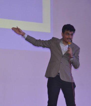 Sahej speaking on stage with a mic